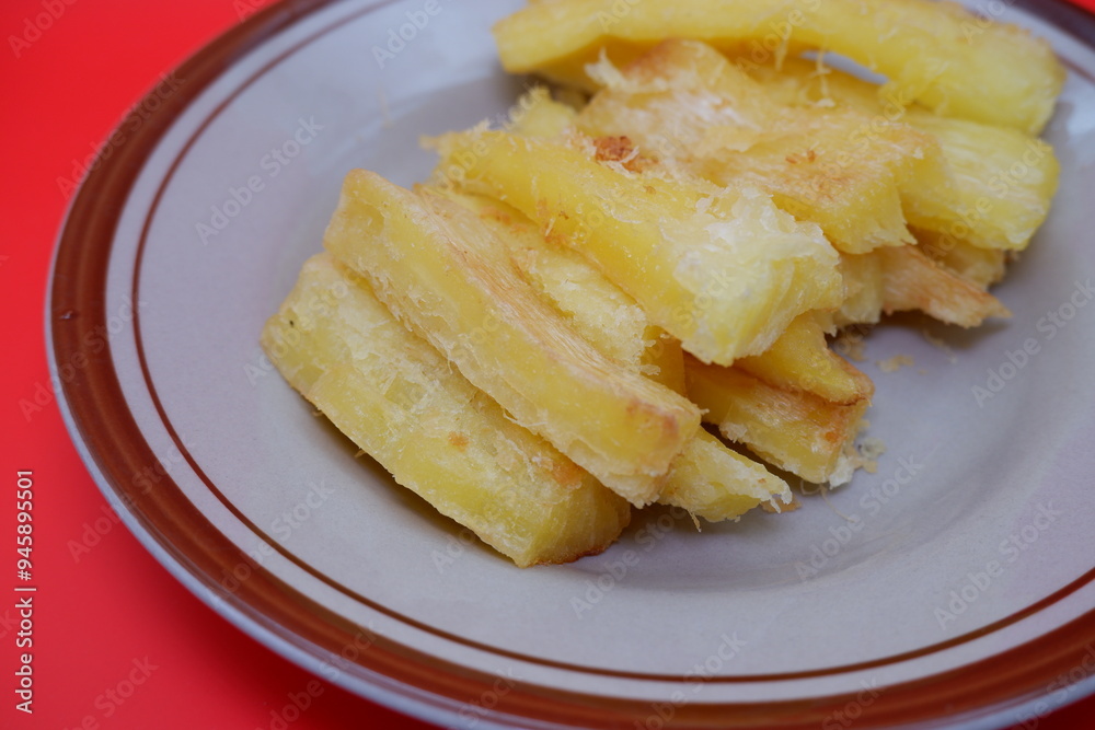 Fried cassava served on a plate. Fried cassava dish isolated on a red background. Fried cassava served on a plate. Fried cassava dish isolated on a red background.
