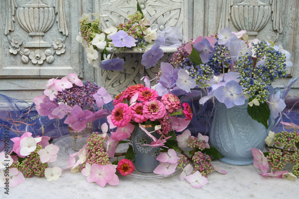 Fototapeta premium Still life of flowers in vases on a marble table with an ornate carved wooden painted background.