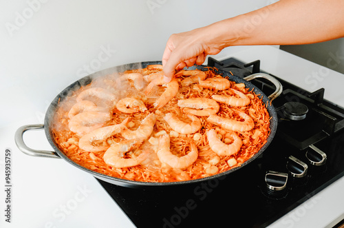 man adding some shrimps to a spanish fideua photo