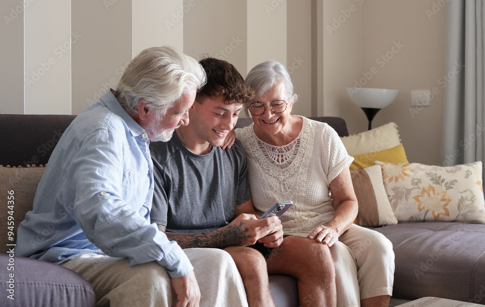Happy Multi generation family of white haired grandparents and young grandson looking at something funny on nephew's mobile phone sitting together at home. Happy Multi generation family of white haired grandparents and young grandson looking at something funny on nephew's mobile phone sitting together at home.