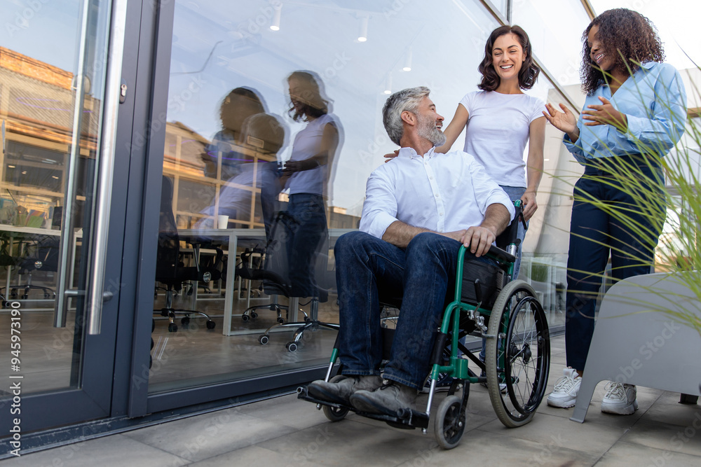 Two women talking to a man on a wheelchair near the office building Two women talking to a man on a wheelchair near the office building