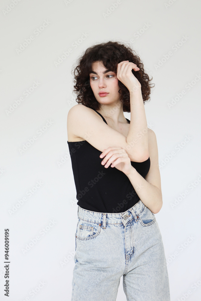 young curly woman in a black tank top posing over light grey background. young curly woman in a black tank top posing over light grey background.