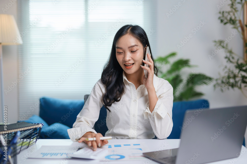 Fototapeta premium Young businesswoman is working from home, talking on the phone and analyzing financial charts