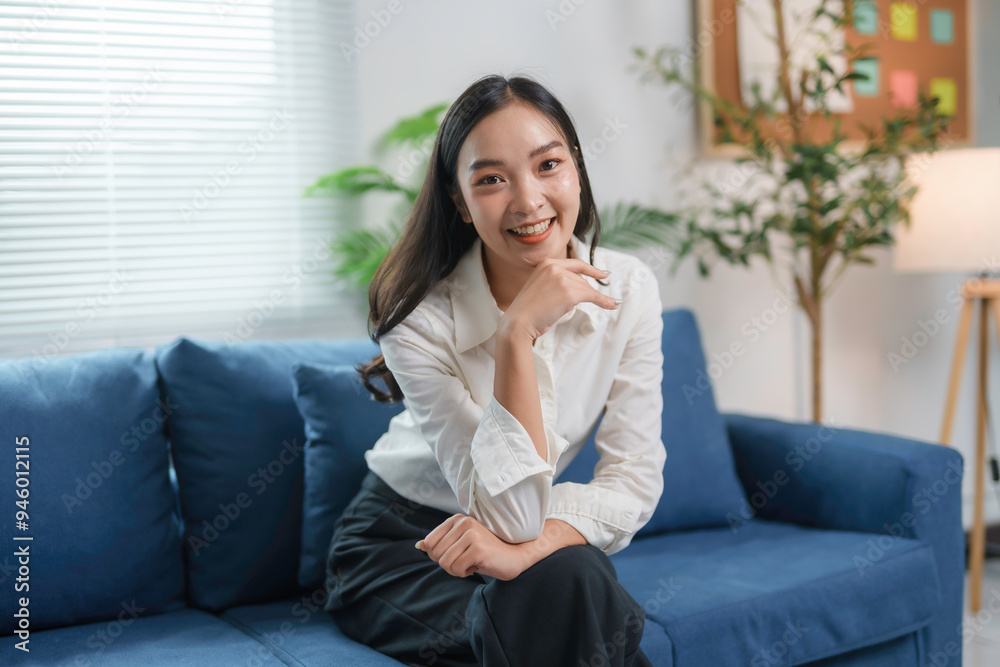 Young asian businesswoman is smiling while sitting on a blue sofa in an office setting Young asian businesswoman is smiling while sitting on a blue sofa in an office setting