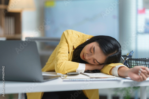 Young asian businesswoman is sleeping at her desk after working on a laptop computer