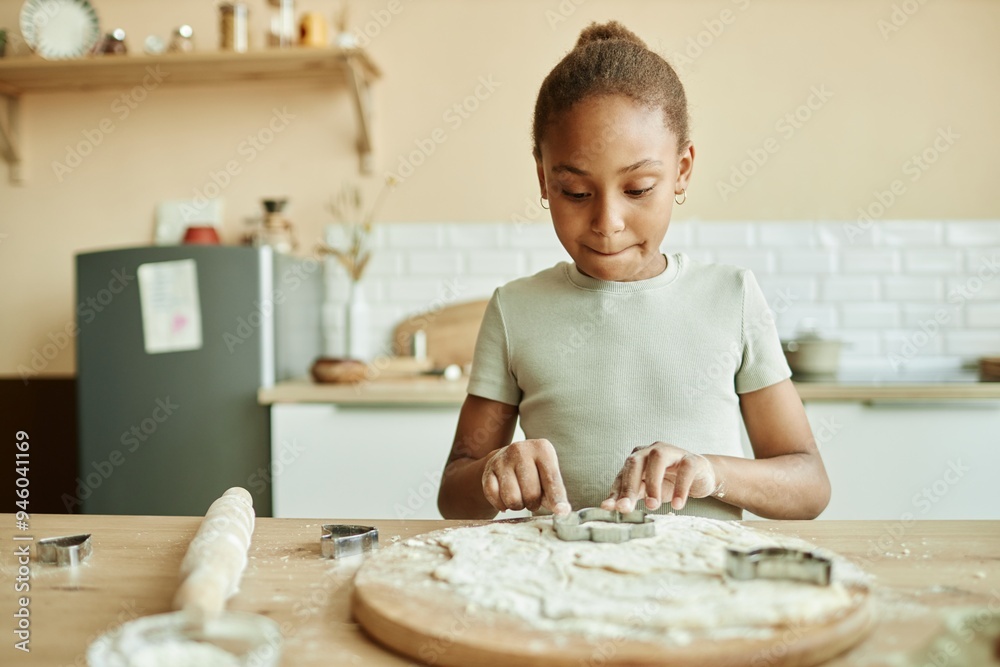 Chest up shot of concentrated African American girl carefully cutting biscuits from dough while cooking homemade pastry on wooden chopping board at cozy beige kitchen, copy space Chest up shot of concentrated African American girl carefully cutting biscuits from dough while cooking homemade pastry on wooden chopping board at cozy beige kitchen, copy space