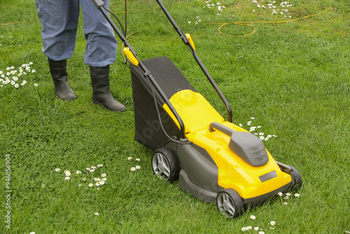 Gardener in black rubber boots trimming lawn with mower 