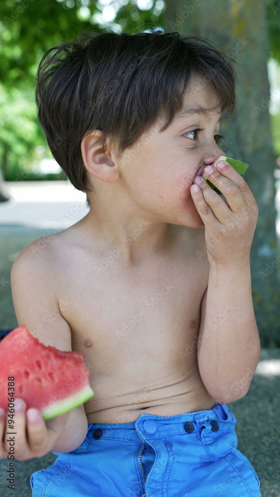 Fototapeta premium Boy enthusiastically eating a slice of watermelon, enjoying the refreshing fruit in a sunny outdoor setting, capturing the joy of summer snacks