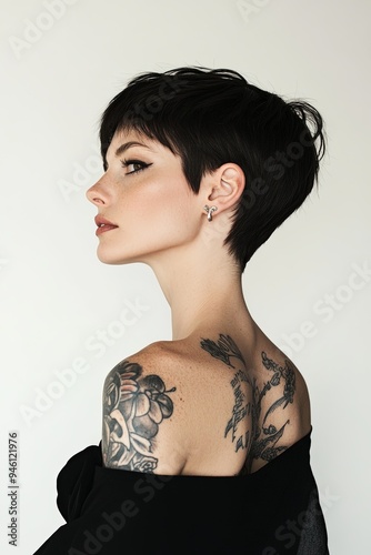 Elegant woman with short dark hair, wearing black and silver, side view with visible tattoos, set against a white background, providing ample copy space and a sophisticated appearance photo