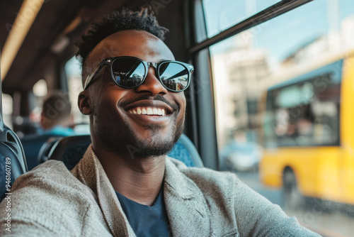 A cheerful Afro-American man in sunglasses is smiling happily while sitting by the window on a bus.