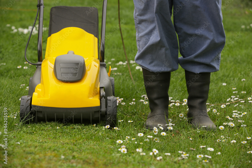 Fototapeta premium Gardener in black rubber boots trimming lawn with mower