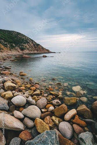 A rocky beach with a view of the ocean and a hill in the background.