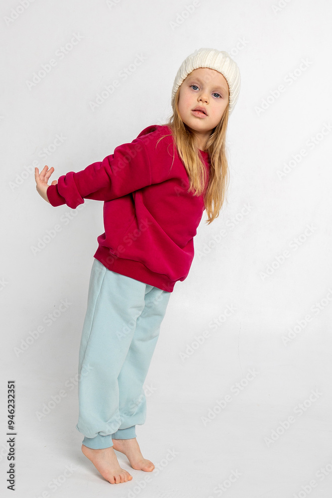 Portrait of beautiful cute little toddler girl. Child with funny face in burgundy color sweatshirt and white hat. Pretty smile kid in studio on light background. Vertical photo Portrait of beautiful cute little toddler girl. Child with funny face in burgundy color sweatshirt and white hat. Pretty smile kid in studio on light background. Vertical photo