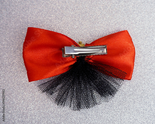 On a gray background lies a bright red bow with a sulfur mesh inverted attached to a metal clip alligator. hair accessories, for dog hair. top view.  photo