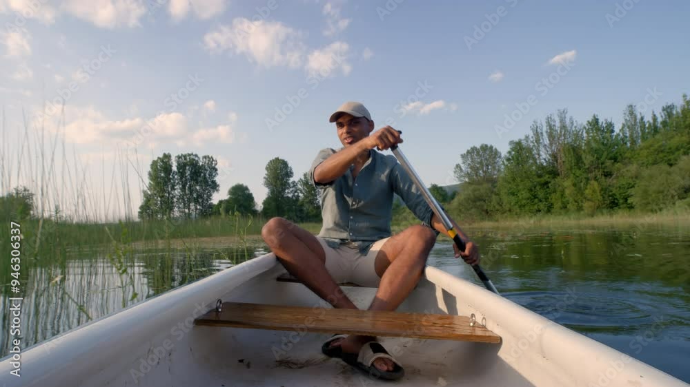 Young man having an active vacation on a beautiful lakeshore, paddling a canoe and enjoying the green landscape, front view.