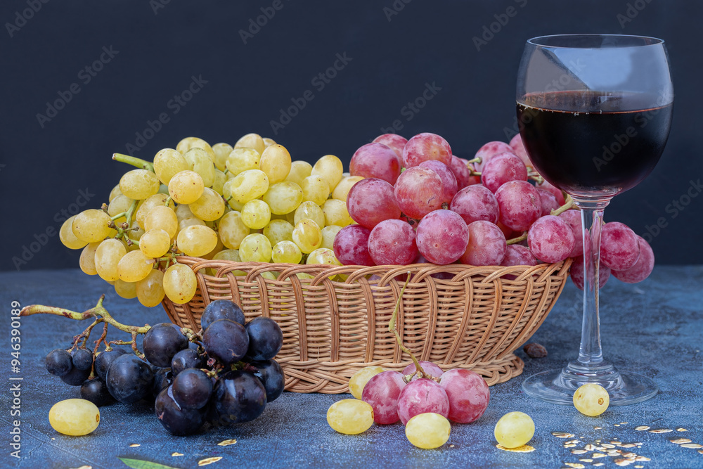 Black grapes on a table, yellow and red grapes in a basket and a glass of red wine on the table