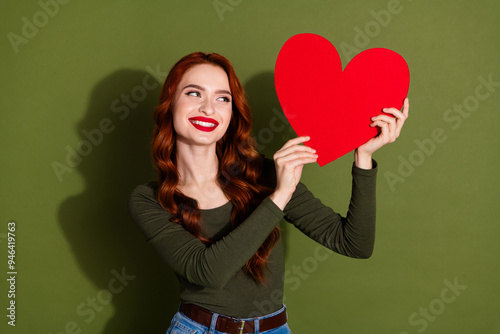 Photo of shiny attractive lady dressed shirt rising big red heart looking empty space isolated green color background