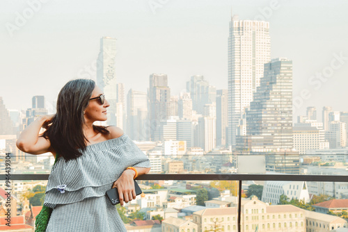 Young pretty woman tourist portrait enjoying Bangkok cityscape skyline panorama. Famous landmark shopping mall over city observation dock. Independent business woman. Side view close up bright filter