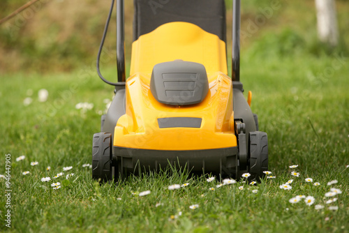 Yellow lawn mower on the spring green grass in the yard