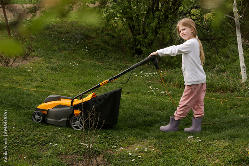 Little girl trimming lawn with mower, helping with houshold chores 