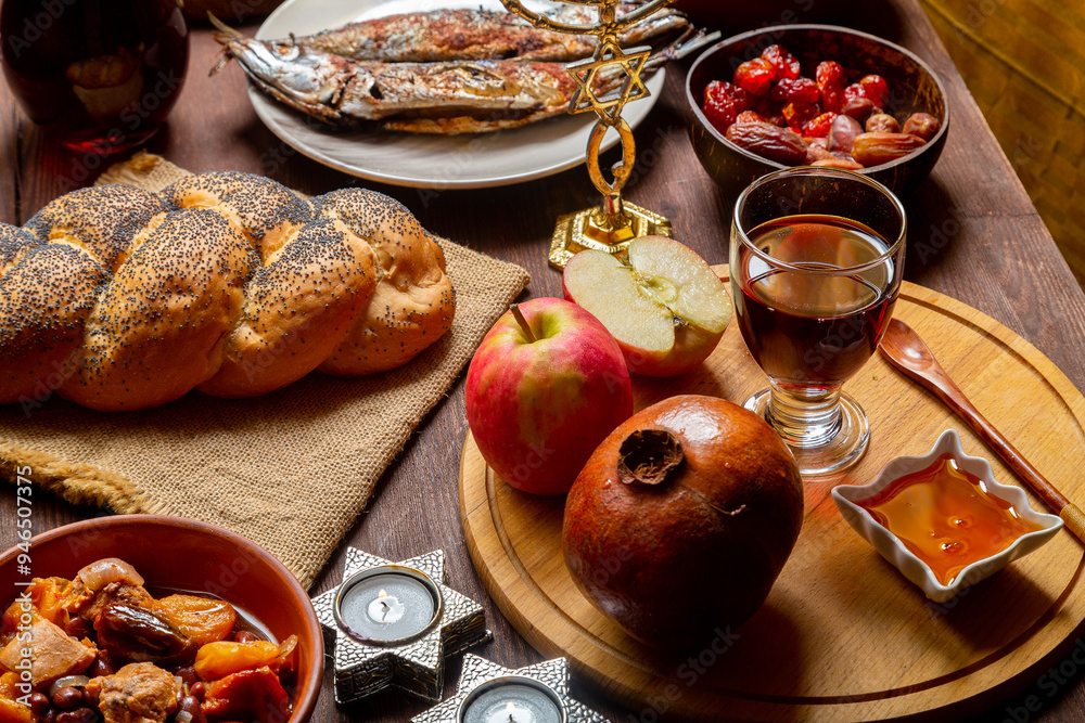 Challah, honey, apple and pomegranate and wine and chelnt on the table with menorah