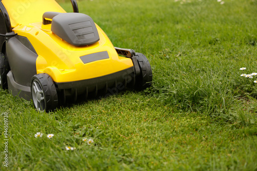 Yellow lawn mower on the spring green grass in the yard