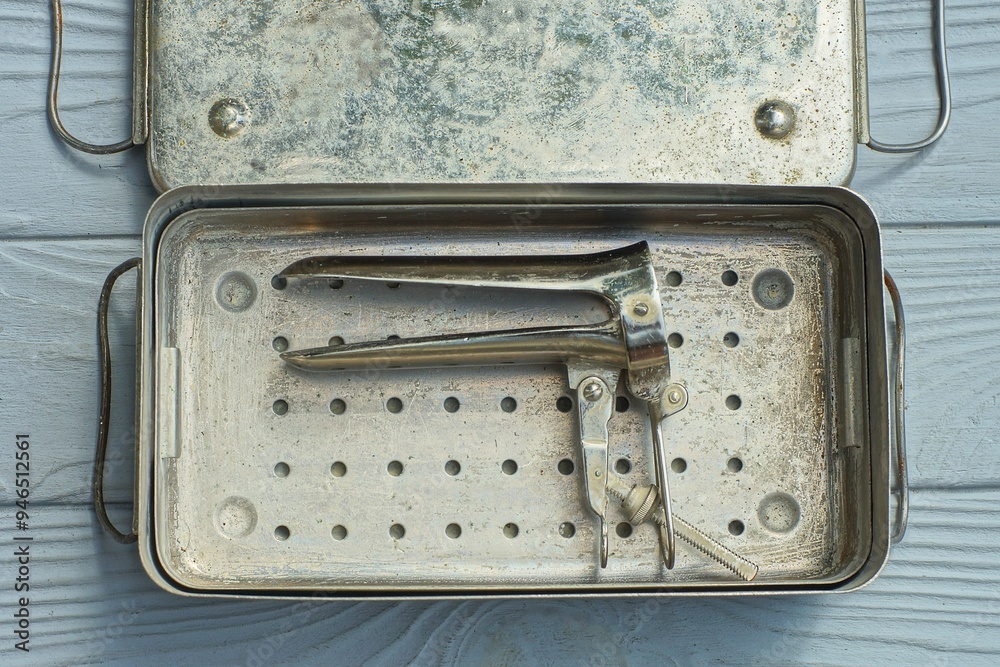 one open iron gray old medical chrome manual vaginal female examination retro clean speculum lies in box with lid on gray wooden table one open iron gray old medical chrome manual vaginal female examination retro clean speculum lies in box with lid on gray wooden table