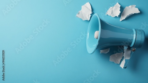 A bright blue megaphone dramatically breaking through pieces of torn blue paper, symbolizing loud announcements, communication and attention-grabbing in design. photo