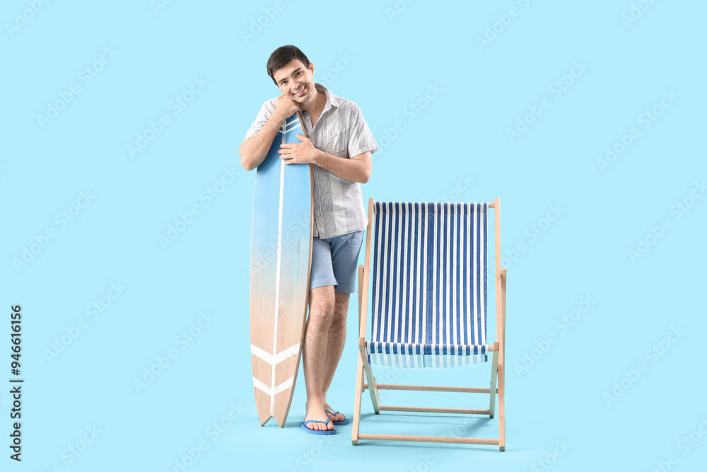 Obraz premium Young man with surfboard and deck chair on blue background