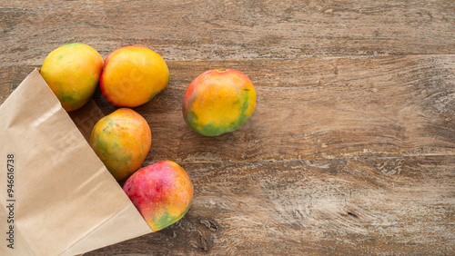 Fototapeta Naklejka Na Ścianę i Meble -  Mango fruits in paper bag over wooden background. Top view.