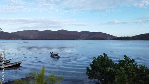 With the radiant sunrise illuminating the sky, a boat cuts through the calm waters of the Caribbean Sea, while towering mountains loom in the distance. photo