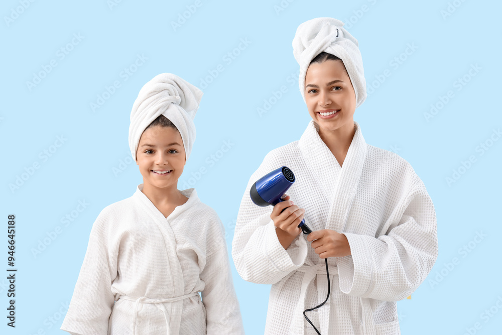 Happy mother with her little daughter in bathrobes and hair dryer on blue background Happy mother with her little daughter in bathrobes and hair dryer on blue background