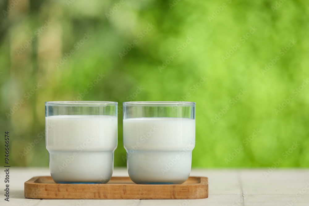 Wooden board with glasses of fresh milk on white tile table outdoors Wooden board with glasses of fresh milk on white tile table outdoors