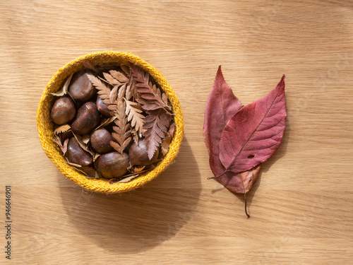 Autumn still life: dry red leaves and a basket with chestnuts and chestnut leaves. All this on a wooden table seen from above