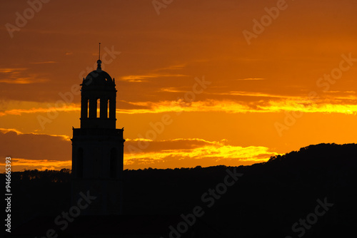Silueta de iglesia tipicamente de pueblo en un atardecer con sol naranja. 