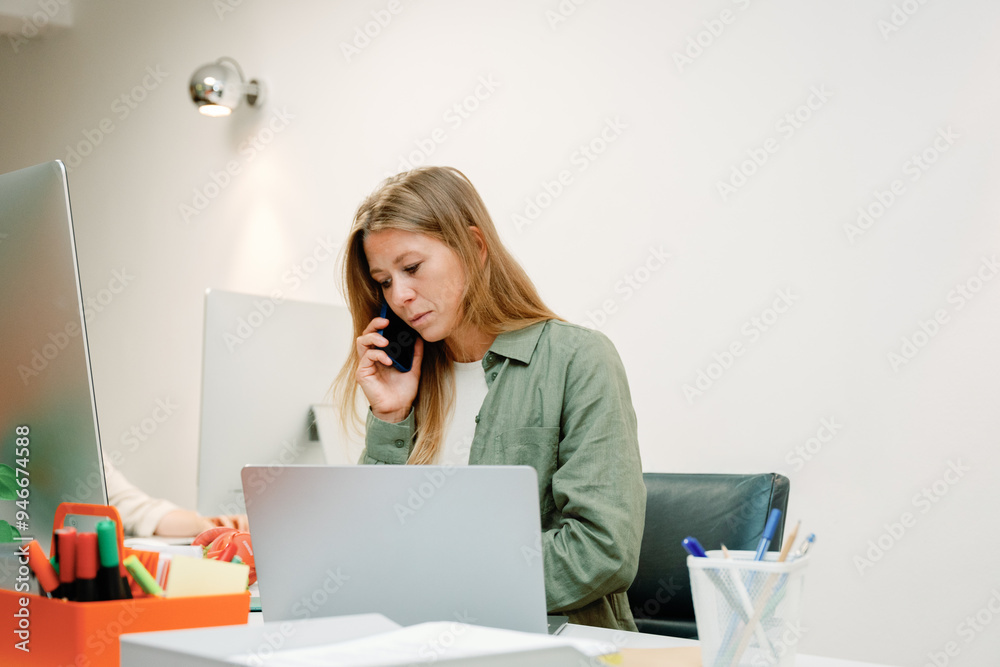 Businesswoman working on a laptop while talking on phone Businesswoman working on a laptop while talking on phone