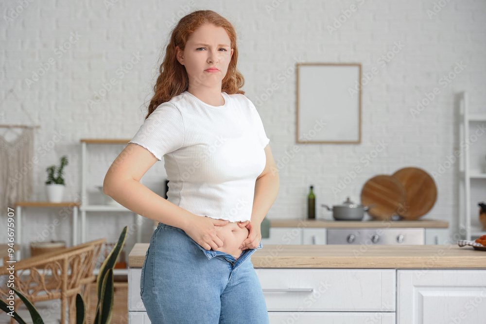 Upset young woman in tight jeans at home. Weight gain concept