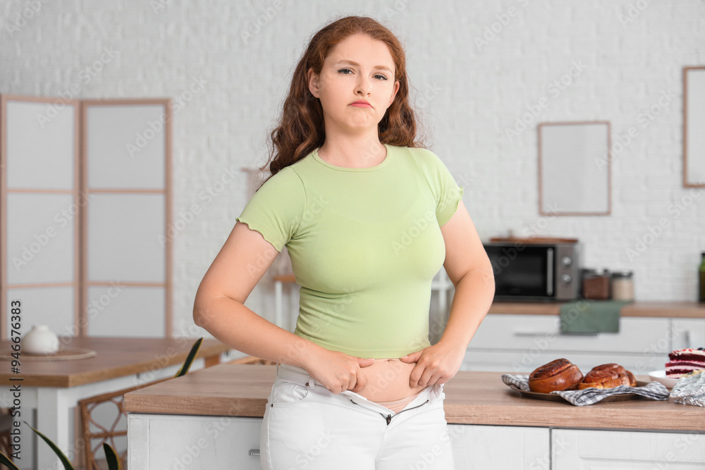 Sad young woman in tight jeans at home. Weight gain concept Sad young woman in tight jeans at home. Weight gain concept