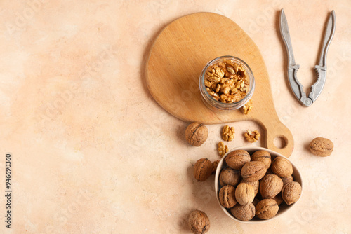 Bowl and jar with tasty walnuts on beige background