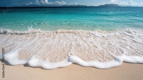 A serene and beautiful sandy beach with crystal clear, calm water extending to the horizon under a bright blue sky dotted with a few fluffy clouds, embodying pure tranquility. photo