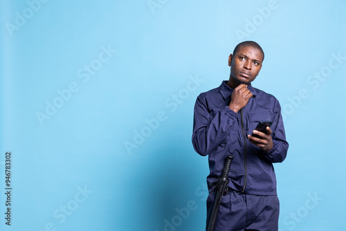 Patrol guard thinking about answers for texts on smartphone, using social media accounts to keep in touch with his friends during his job duty. Male agent checks messages online in studio. photo