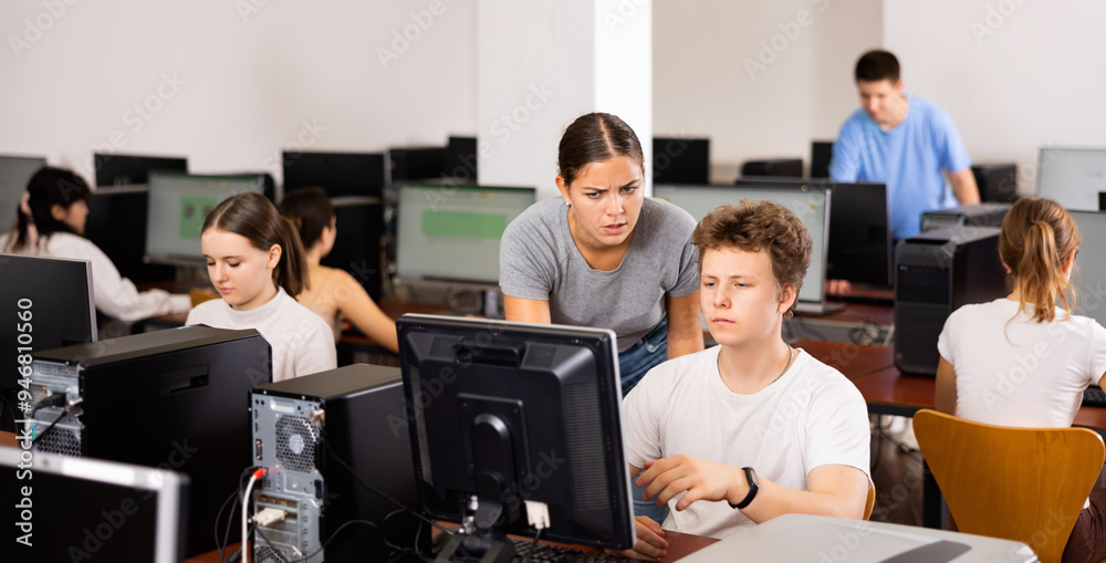 Fototapeta premium Schoolboy using computer and teacher helping to him in classroom