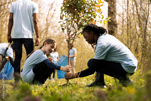 Two diverse activists working together to plant more trees and greenery, filling up ground holes and growing vegetation. Kid and teenager girls collaborating on preserving the environment.