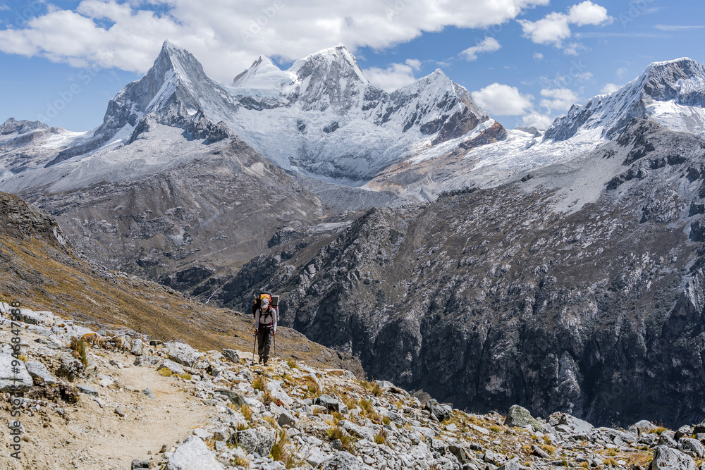 woman walks with a backpack in the middle of a mountainous landscape with snowy peaks in the background of the landscape and carrying technical mountaineering and climbing equipment woman walks with a backpack in the middle of a mountainous landscape with snowy peaks in the background of the landscape and carrying technical mountaineering and climbing equipment