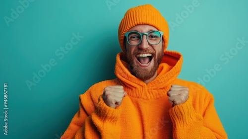 A joyful man dressed in orange clothes and glasses, energetically shouting with excitement and making a fist-pump gesture, showcasing his vibrant personality indoors. photo