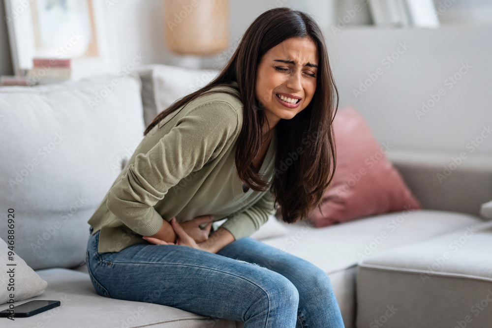 Unhealthy young woman with stomachache leaning on the couch in the living room at home. Unhealthy young woman with stomachache leaning on the couch in the living room at home.