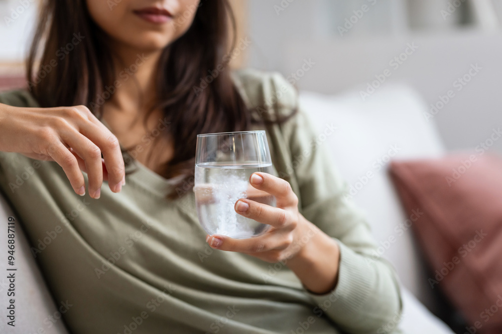 Unhealthy young woman dropping an effervescent pill into the glass of water at home Unhealthy young woman dropping an effervescent pill into the glass of water at home