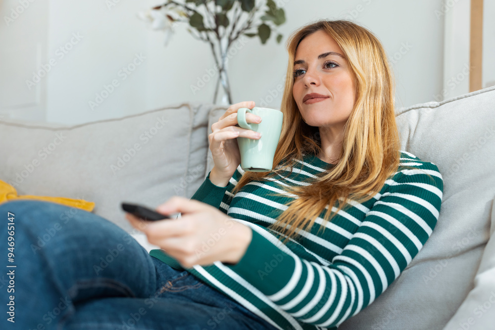 Pretty young woman turning on the tv while drink coffee on sofa at home Pretty young woman turning on the tv while drink coffee on sofa at home