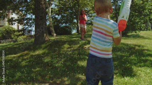 A young boy and girl enjoy a playful water gun fight in the yard on a hot summer day. The splashes of water and their laughter fill the air, capturing the joy of cooling off in the summer heat.