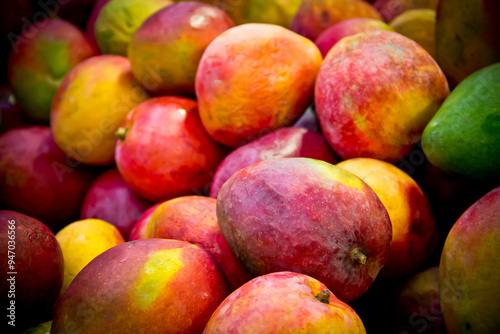 Tropical fresh mangoes staked at a market stall, close-up.